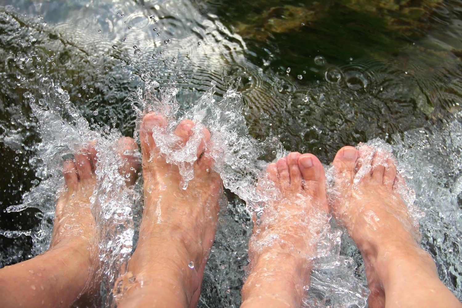 Zwei Paar Füße im kalten und sprudelnden Flusswasser, Erfrischung und Abhärtung nach Kneipp