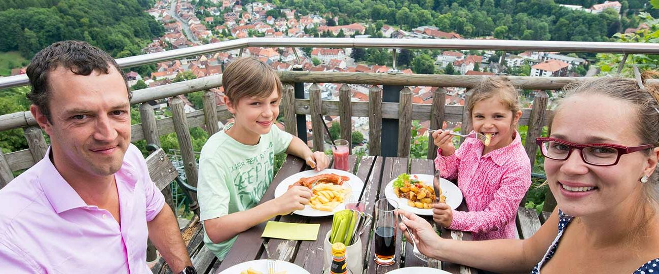Eine Familie genießt Currywurst und Schnitzel auf der Terrasse der Berggaststätte Hausberg.